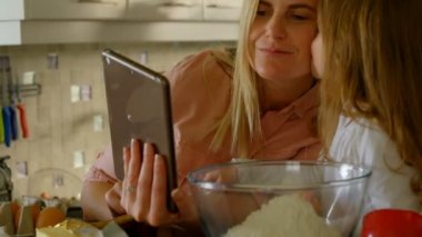 Bir anne ve kızı evde yemek hazırlarken dijital tablet kullanarak kapatın. Küçük kız öpmek annesi o Internet üzerinde tarifi için seyir ederken.