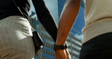 Düşük açılı dikiz şehir caddede yürüyüş ve güneşli bir ağır çekimde el ele tutuşarak çekici çift