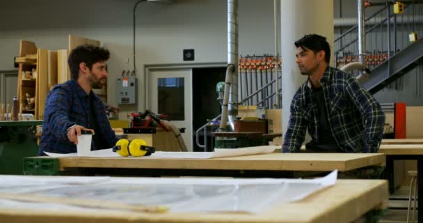 Front view of young carpenters sitting down and interacting with each other in workshop while having coffee