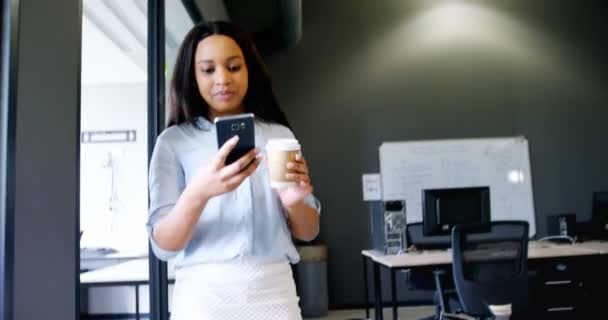 Vue à angle bas d'une jeune femme d'affaires mixte assez attrayante et bien habillée qui boit du café et utilise un téléphone portable au bureau. Le groupe multiethnique de collaborateurs travaille sur leurs ordinateurs .