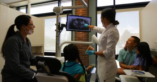 歯科医療センターの多民族の患者に歯科用レントゲン検査報告書を説明する白い実験室のコートを身に着けている女性歯科医の後姿 — ストック動画