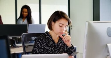 Önden görünüm Office masasında cep telefonuyla bir genç güzel kadın Yönetim Kurulu üyesiydi. Co-işçiler arka planda konuşurken çok etnik gruptan oluşan grup.