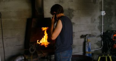 Kadın metal ateşin önünde fabrikasında çalışırken cep telefonu üzerinde konuşurken arka görünümü.