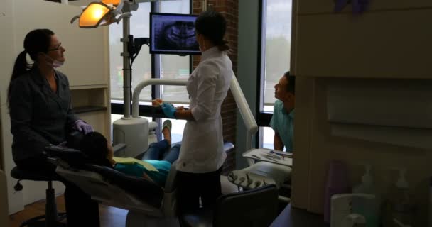 广泛的观点 熟练的女牙医解释牙科 光报告病人在诊所 当牙医向他的女儿解释时 父亲在看 — 图库视频影像