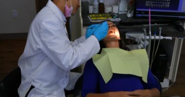 Bir kadın hastada klinik inceleyerek Asya erkek diş hekimi yan görünüm. Diş hekimi onu araçlarıyla incelerken ağzını açma hasta.