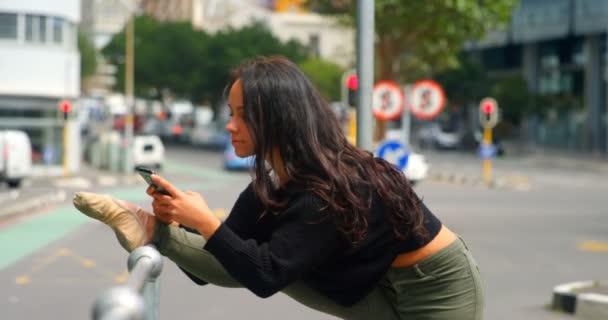 美丽的女人在城市的栏杆上伸展腿时 用手机使用手机 城市在背景4K — 图库视频影像