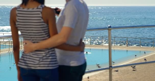 手すりの近くに携帯電話のカップル撮影 Selfie の背面します バック グラウンドで美しい海の景色 — ストック動画