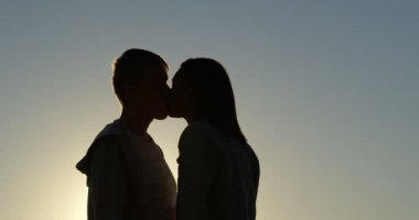 Gün batımında romantik çift öpüşme yan görünüm. 4k arka planda gökyüzü günbatımı