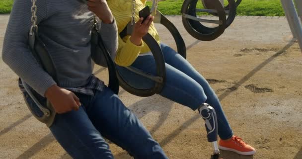 在公园里用手机的幸福夫妇 夫妇坐在操场秋千4K — 图库视频影像