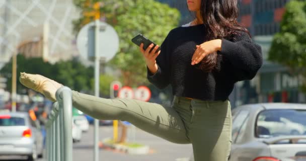 Hermosa Mujer Usando Teléfono Móvil Mientras Pierna Estira Una Barandilla — Vídeos de Stock