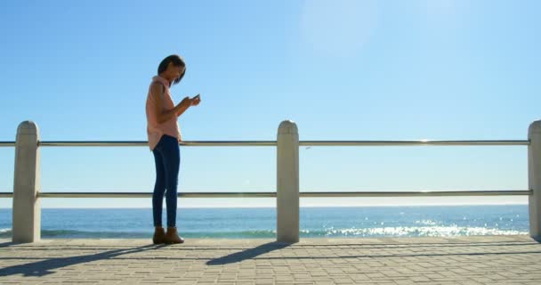 年轻女子站在长廊上使用手机 美丽的天空和平静的大海在 Beackground — 图库视频影像