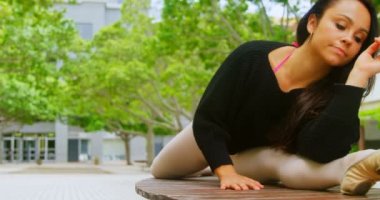 Genç balerin pratik bale dans parkta bankta. 4k planda yeşil ağaçları