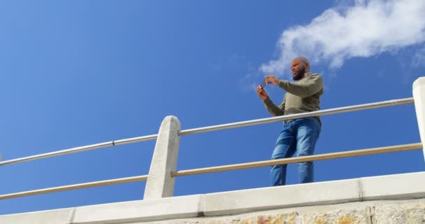 男子在栏杆附近用手机拍照的低角度视图 背景中的天空和云4K — 图库视频影像