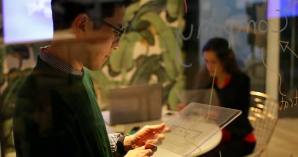 男性高管在办公室使用数字平板电脑时在玻璃板上写作 同事们在4K 的背景下相互互动 — 图库视频影像