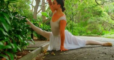 Kadın balerin parkta germe egzersiz yapmak. 4k planda yeşil ağaçlar