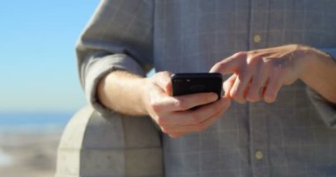 Gezinti yerinde cep telefonu kullanan adam orta bölümü. Ayakta deniz kıyısından 4k