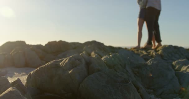 浪漫的年轻夫妇在海滩上拥抱在岩石上 夫妇看着大海4K — 图库视频影像