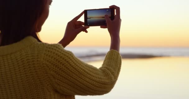 携帯電話の夕日をキャプチャ美しい女性のリアビュー 穏やかな海とバック グラウンド で劇的な空の景色 — ストック動画