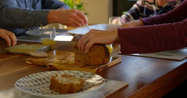 Femme coupant du pain sur la table à manger. Famille assise ensemble pour le petit déjeuner 4k 
