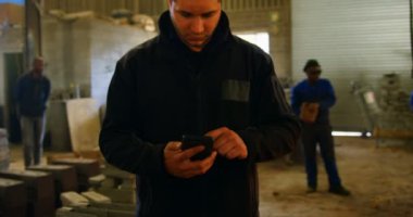 Erkek işçi cep telefonuyla atölyede. 4 k arka planda çalışma arkadaşları