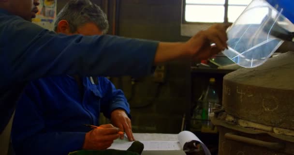 男性ワーカー鋳造ワーク ショップでクリップボードに書き込みます の背景に立っている同僚 — ストック動画