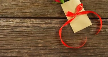 Ahşap yüzey üzerinde kırmızı kurdele ile zarf üzerinde kırmızı gül buketi. Sevgililer günü kavramı 4k