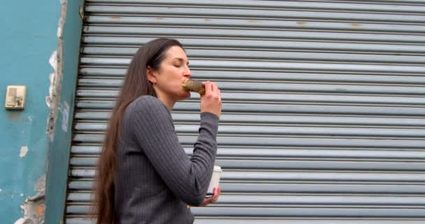 街を歩きながらドーナツを持つ美しい女性 使い捨てカップ を保持している女性 — ストック動画