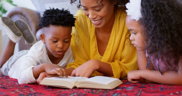 快適な家で本を読んで彼女の子供と母親が黒のフロント ビュー 黒母娘と息子の を家でのんびりと — ストック動画