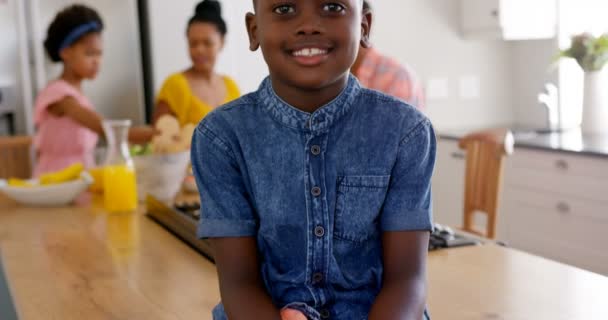 Čelní pohled šťastné černý chlapec při pohledu na fotoaparát. Černá rodina jíst potraviny v pozadí 4k