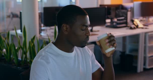 若い男性の幹部は 現代のオフィスで机の上の作業中にコーヒーを飲んでいます の机の上に座っている若い男性エグゼクティブ — ストック動画