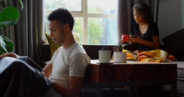 デジタル タブレットを使用して 自宅のリビング ルームで若いアジア人の側面図です 若いアジアの女性は 自宅のリビング ルームで携帯電話を使用して — ストック動画