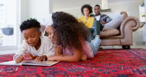 リビング ルームの快適な家で絵本を読んでかわいい黒い子供の正面 母と父の のソファでリラックス — ストック動画