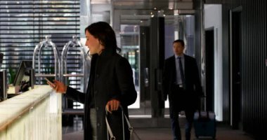 Beyaz işkadını otel resepsiyonunda cep telefonu kullanarak yan görünüm. Otelin 4 k Asya işadamı girer