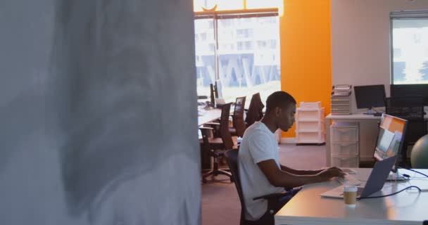 近代的なオフィスのデスクでコンピューター上の黒の男性エグゼクティブ働く若いの側面図です 若い黒男性エグゼクティブ座っている の机の上 — ストック動画