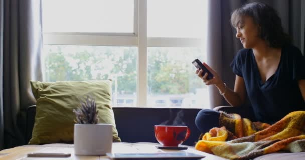 自宅携帯トウモロコシパンを使用して若いアジア女性の正面から見た図 のリビング ルームのソファの上に座っている若いアジア女性 — ストック動画
