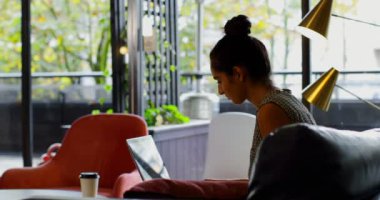 Modern ofis içinde laptop üzerinde genç beyaz kadın yönetici çalışıyor yan görünüm. Kadın yönetici 4 k kanepede rahatlatıcı
