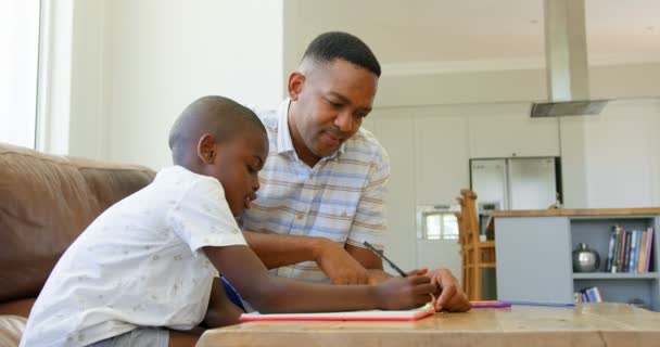 黑人父亲在家里帮儿子做作业的侧视图 坐在4K 桌旁的黑人父子 — 图库视频影像