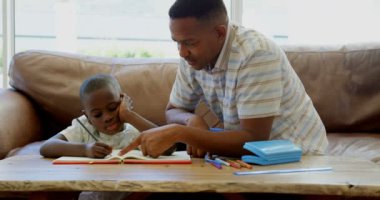 Siyah baba oğlu evde ev ödevlerinde yardımcı önden görünümü. Siyah baba ve oğul 4 k masada oturan