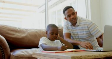 Siyah baba oğlu evde ev ödevlerinde yardımcı önden görünümü. Dizüstü bilgisayar ev 4 k kullanarak siyah baba