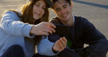 Genç beyaz kaykaycı çift alarak selfie cep telefonu ülke Road ile önden görünümü. Onlar birlikte 4 k ışığında yolda oturuyorlar