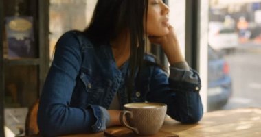 Genç Asyalı kadın Cafe pencereden bakarak önden görünümü. 4 k kafede masada oturan genç düşünceli Asyalı kadın