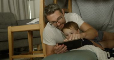 Beyaz baba ve oğul rahat bir ev dijital tablet kullanarak önden görünümü. Baba ve oğul yerde 4 k