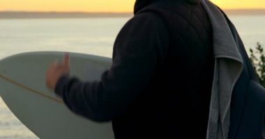 Sörf tahtası ayakta Sahil yakınındaki yetişkin beyaz adamla yan görünüm. Deniz günbatımı sırasında 4 k görünen adam