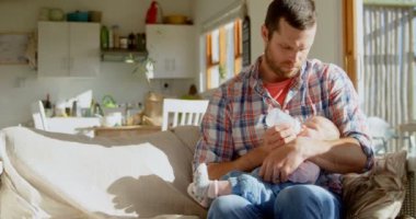 Önden görünüm bir orta yetişkin beyaz baba süt onun bebek besleme şişe içinde rahat bir ev. 4 k ışığında kanepede oturan babası