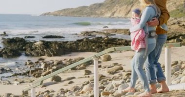 Beyaz aile güneşli bir günde kumsalda yürürken yan görünüm. Bir askı 4 k içinde taşıma bebek anne