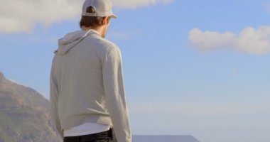 Arkadan Görünüş Genç beyaz adam sahilde duran ve denize bakarak. Kaykay güneş 4 k tutan adam