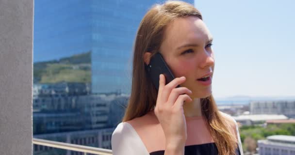 年轻的高加索女商人在现代办公室的阳台上用手机说话的侧视图 站在阳台上的女商人4K — 图库视频影像