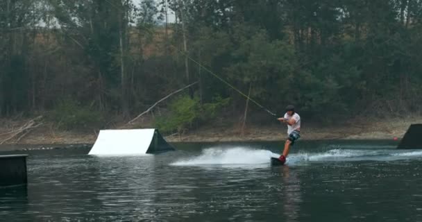 市湖でウェイク ボードのトリックを行う白人の若い男のフロント ビュー 競技者がウェイク ボード ロープ — ストック動画