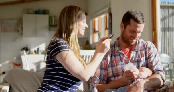 中成人白种人母亲点击照片 而父亲喂养牛奶他的婴儿从奶瓶在家里 母亲使用手机4K — 图库视频影像