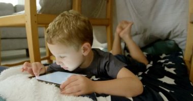Önden görünümü dijital tablet içinde rahat bir ev kullanarak sevimli beyaz çocuk. 4 k yerde yatarken çocuk